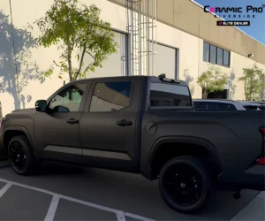 Side profile view of a matte black pickup truck parked alongside an outdoor parking bay.