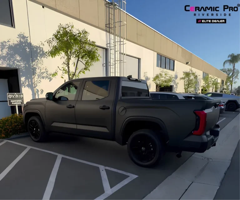 Matte black pickup truck parked in a marked parking space outside an industrial building.